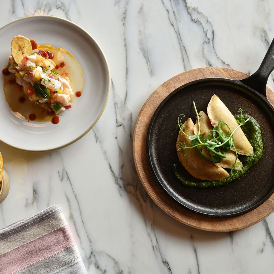 Lobster ceviche and a golden empanada elegantly presented on a marble surface.